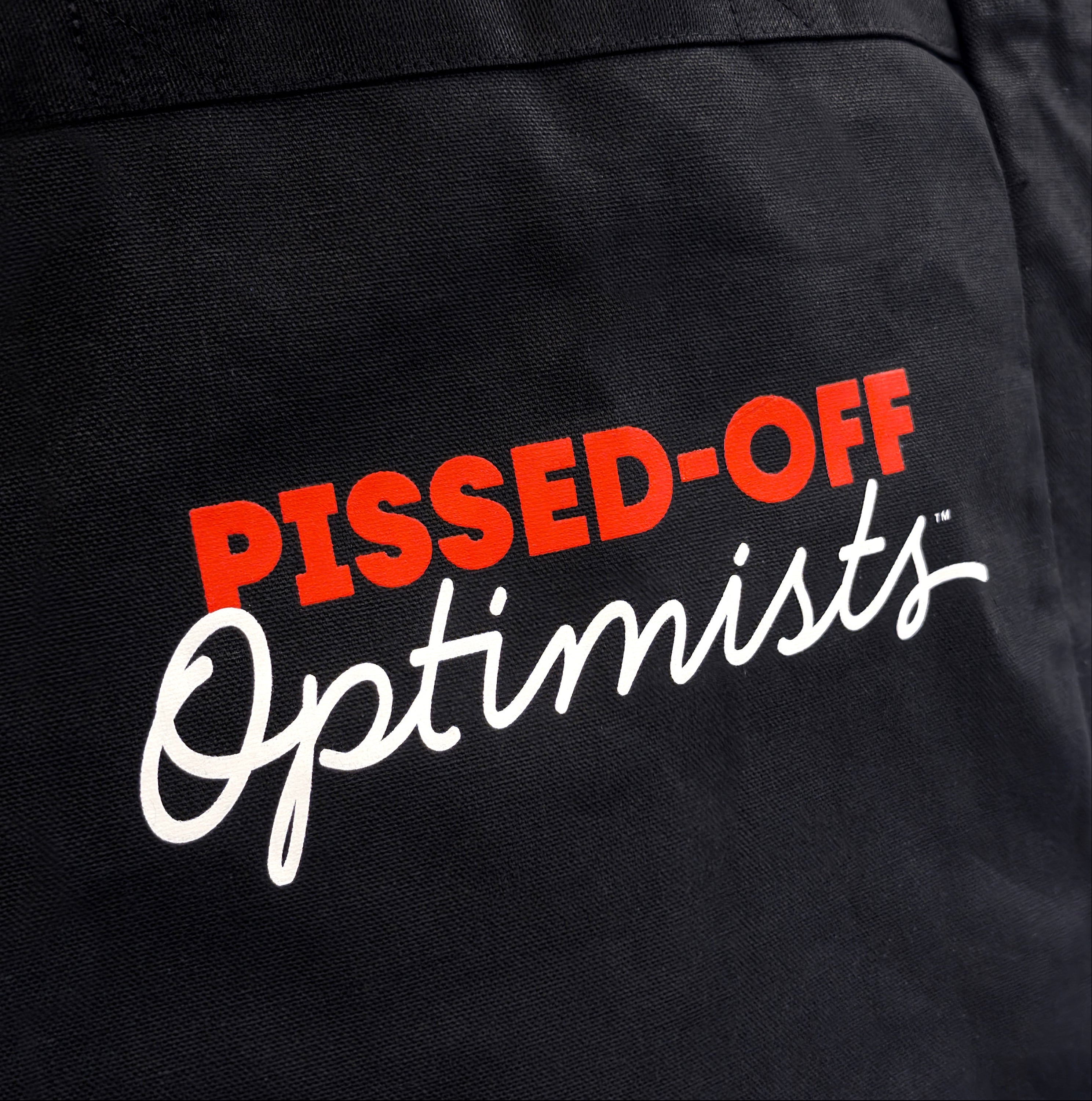 Black apron with 'PISSED-OFF Optimists' text in red and white on a black background