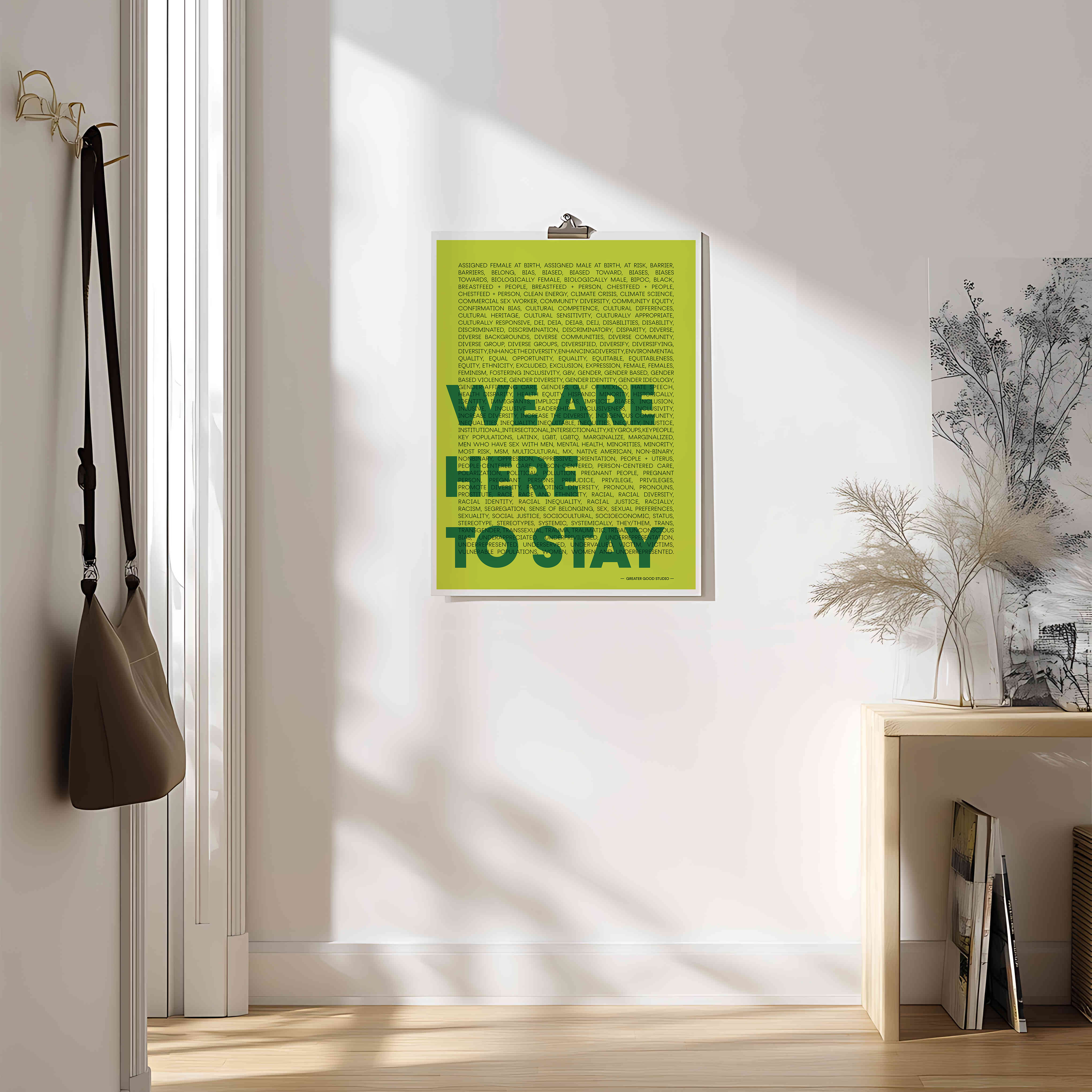 Green poster with 'WE ARE HERE TO STAY' text on a wall in a room with a plant and a bag.